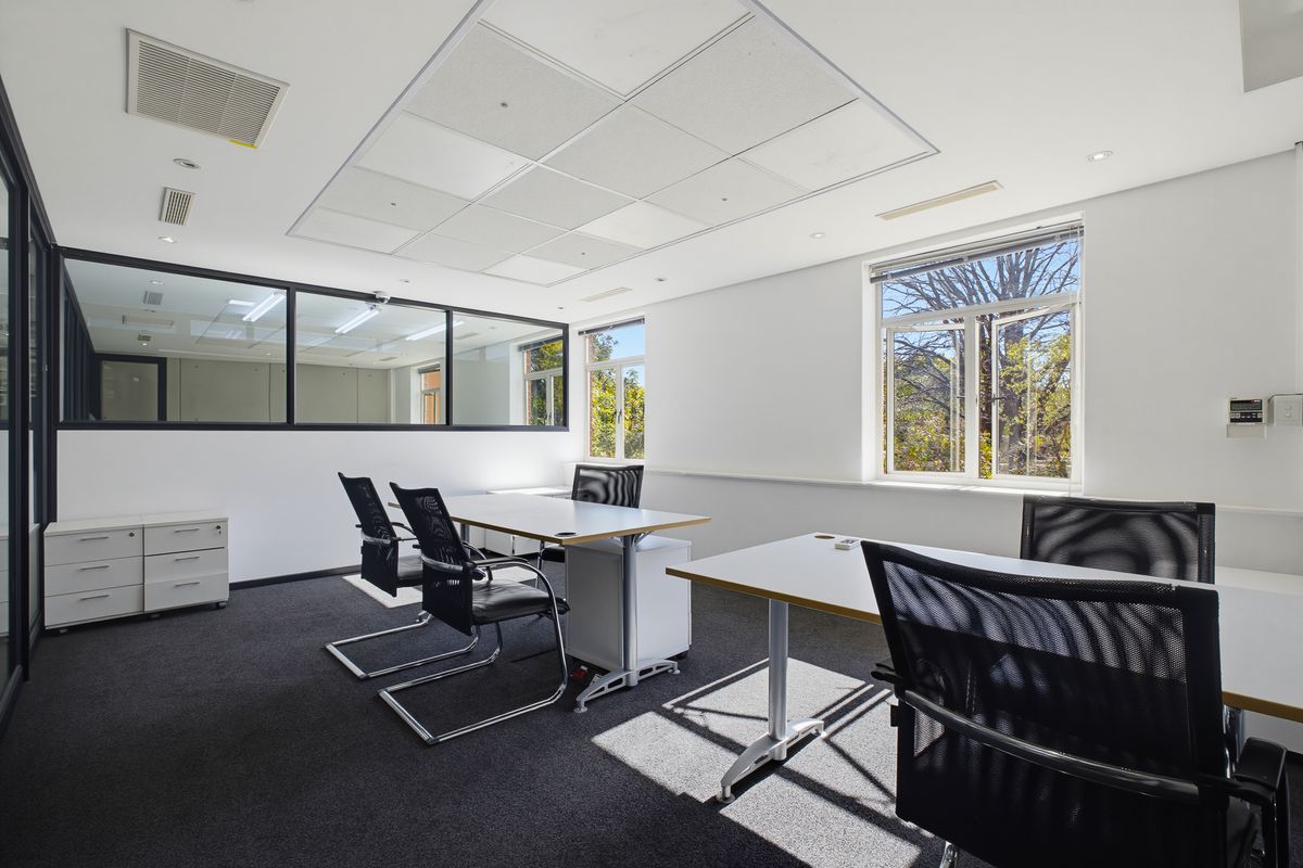 A bright, professional office space featuring a suspended ceiling, glass partition wall, and large windows providing natural light and exterior views.