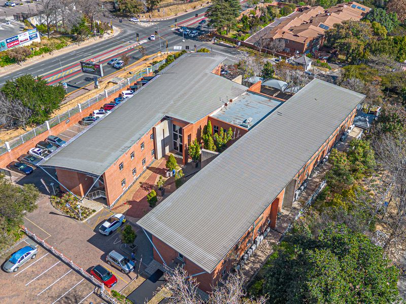 Aerial view of a multi-story brick office complex featuring metal roofing, paved parking facilities, and surrounding landscaped grounds.