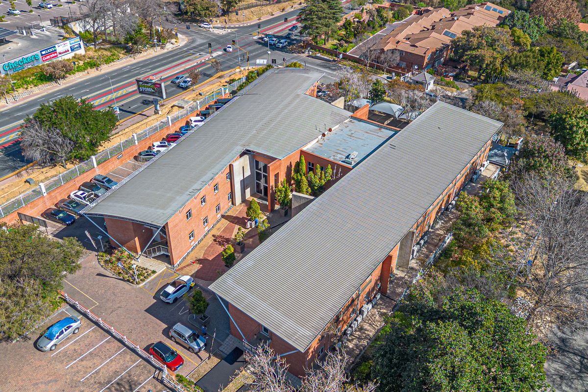 Aerial view of a multi-story brick office complex featuring metal roofing, paved parking facilities, and surrounding landscaped grounds.