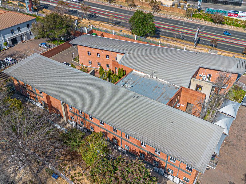 Aerial view of a multi-story brick office complex featuring corrugated metal roofing, external air conditioning units, and an adjacent paved parking area.