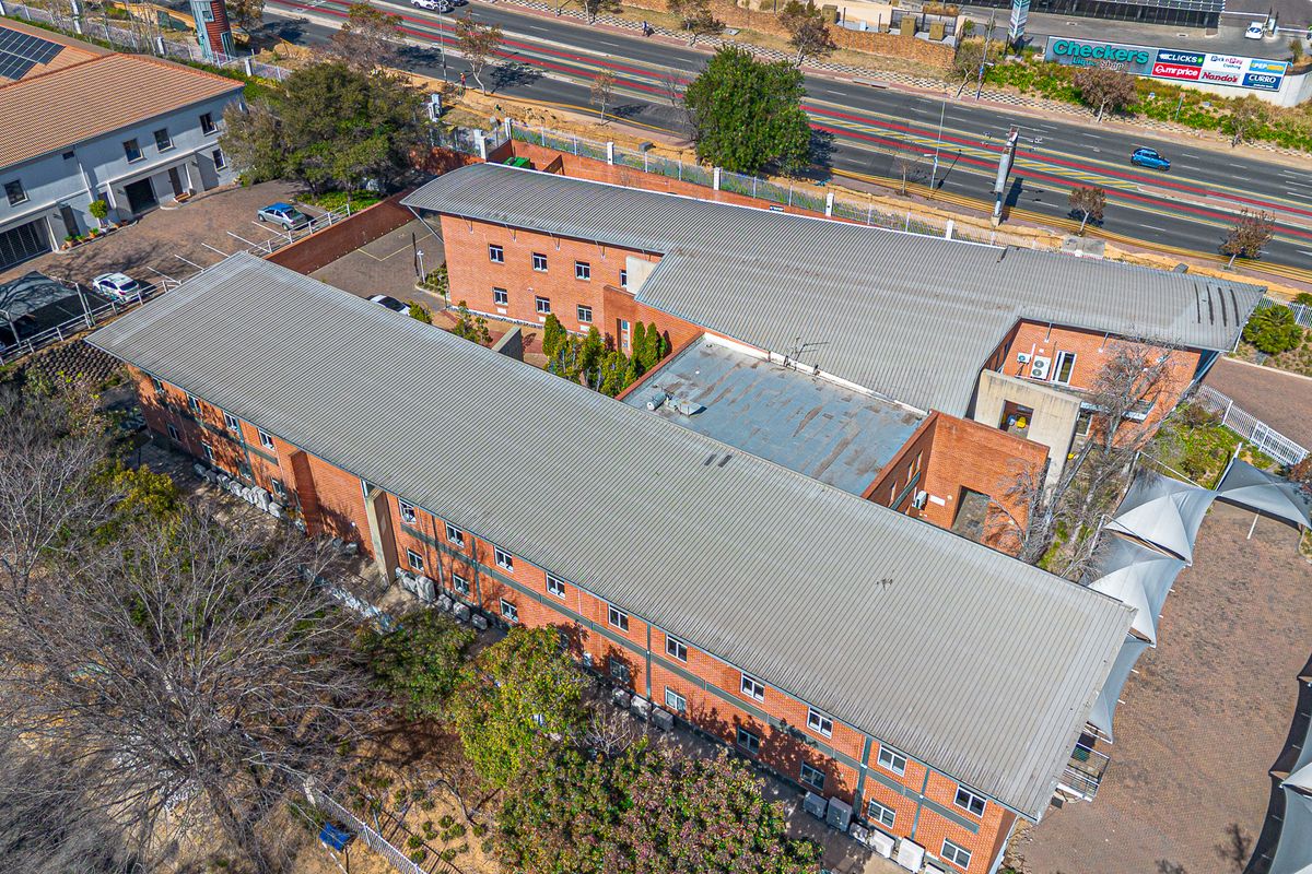 Aerial view of a multi-story brick office complex featuring corrugated metal roofing, external air conditioning units, and an adjacent paved parking area.