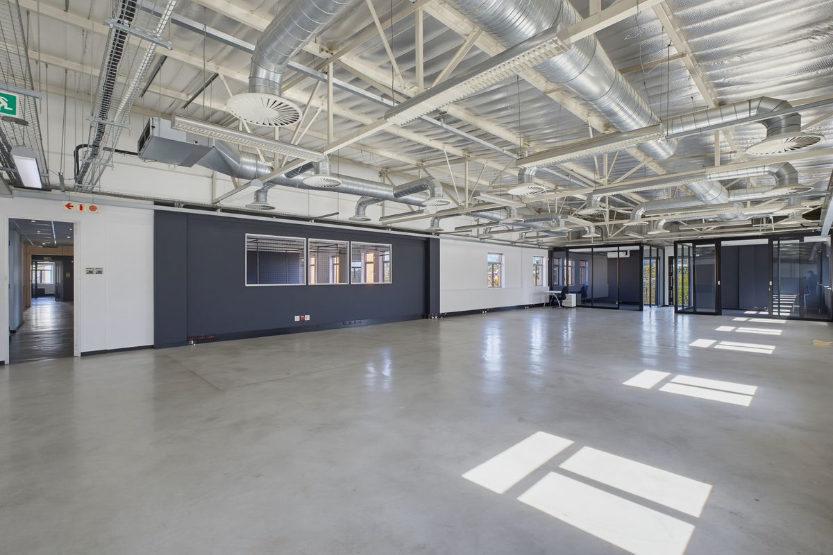Spacious open-plan office area featuring polished concrete floors, exposed industrial-style ceiling with HVAC ducting, and modern glass partitions.