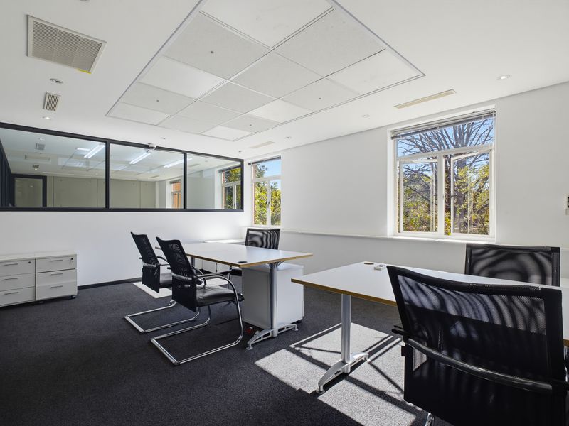 A bright, professional office space featuring a suspended ceiling, glass partition wall, and large windows providing natural light and exterior views.