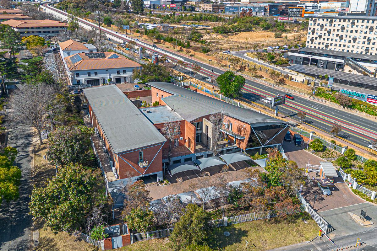 Aerial view of a modern office complex featuring brick architecture, metal roofing, solar panels, and a paved parking area with shade cloth carports.