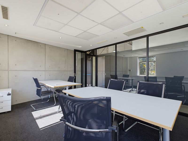 Modern office space featuring exposed concrete wall panels, glass partitioning, and a suspended ceiling with integrated air conditioning.