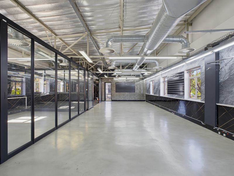 Modern open-plan office space featuring polished concrete floors, exposed industrial ductwork, glass partitions, and contemporary marble-effect wall finishes.