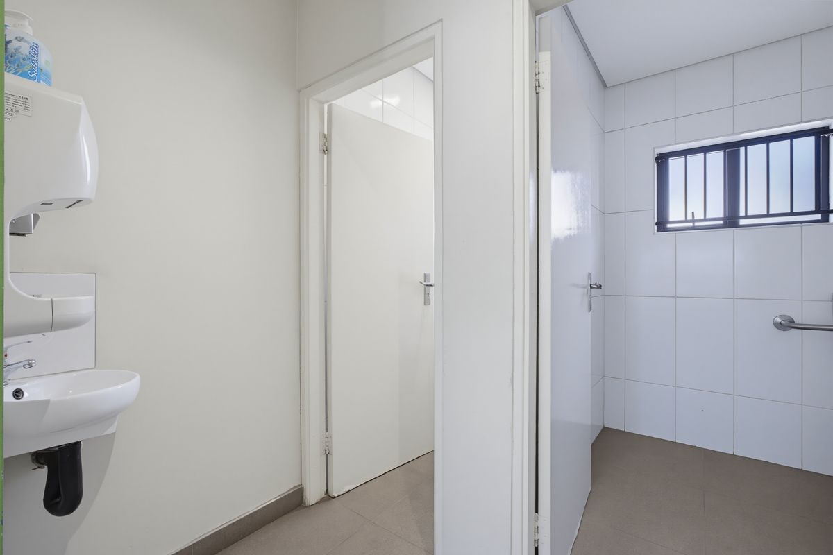A clean, functional commercial bathroom featuring tiled walls, a wall-mounted basin, and a secure window with safety bars.