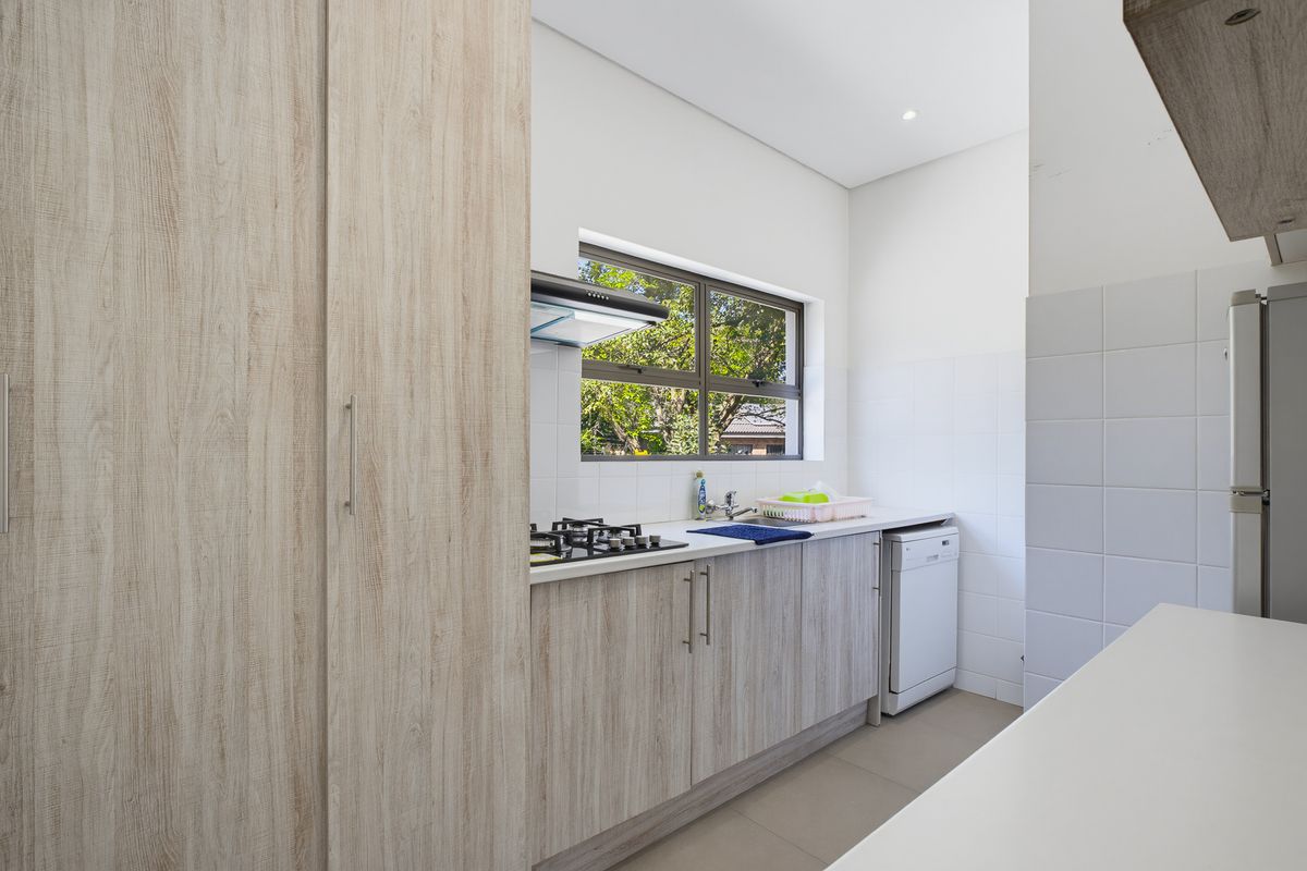 A modern, well-maintained kitchen featuring light wood-grain cabinetry, a gas hob with extractor, tiled splashbacks, and neutral floor tiles.