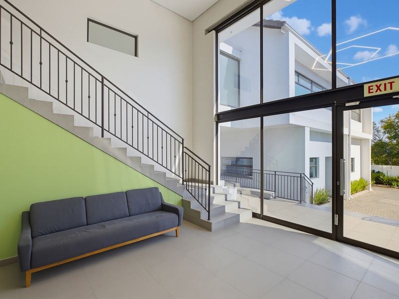 Bright and modern commercial entrance foyer featuring a staircase, large floor-to-ceiling windows, and tiled flooring with direct access to the exterior.