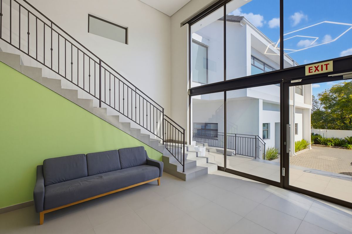 Bright and modern commercial entrance foyer featuring a staircase, large floor-to-ceiling windows, and tiled flooring with direct access to the exterior.