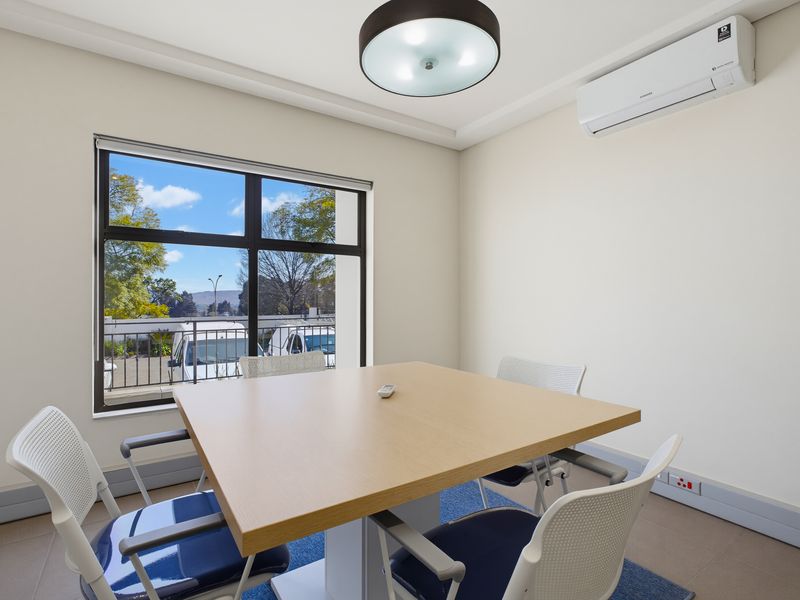 A bright and professional office space featuring a large window, split-system air conditioning, and neutral finishes, suitable for a productive work environment.