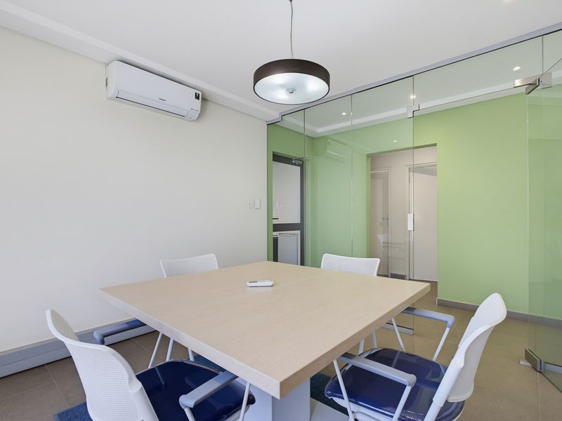 A modern office meeting room featuring a glass partition wall, tiled flooring, and a wall-mounted split-system air conditioner.
