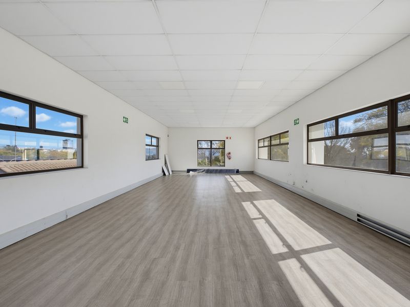 A bright, vacant commercial office space featuring vinyl flooring, a suspended ceiling, and large windows providing ample natural light.