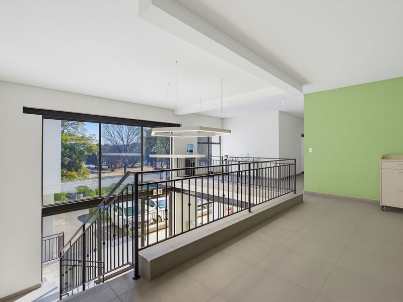 Spacious commercial hallway featuring tiled flooring, a metal balustrade overlooking the lower level, and large windows providing ample natural light.