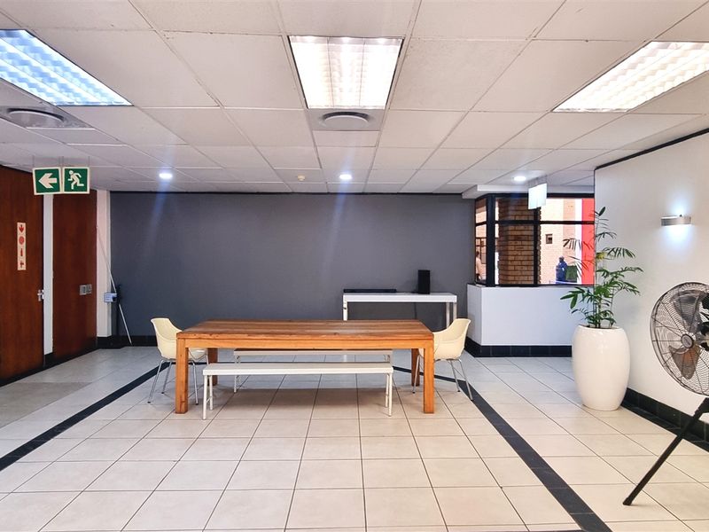 A spacious office area featuring a suspended acoustic ceiling, tiled flooring, and multiple access doors, suitable for a collaborative workspace or reception area.