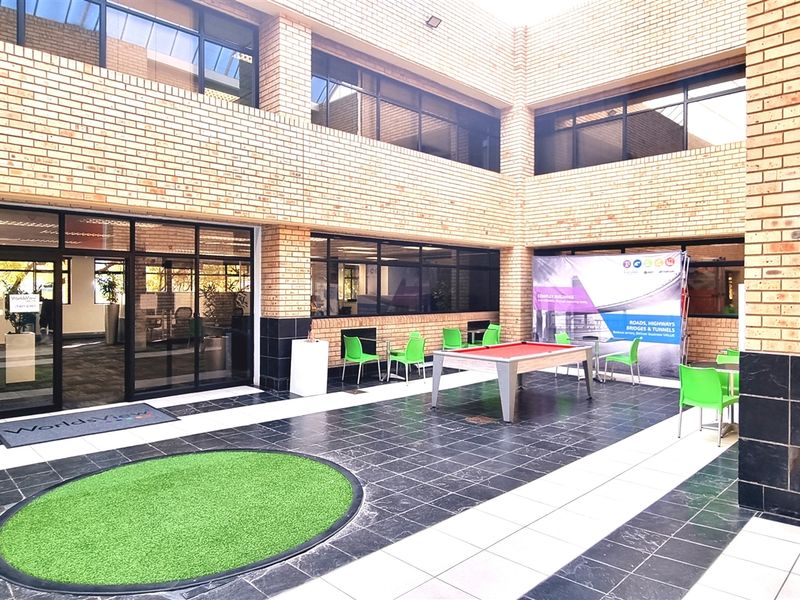 A modern office courtyard featuring a paved patio area with brick facade, large glass windows, and integrated outdoor seating space.