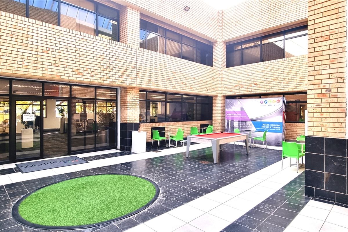A modern office courtyard featuring a paved patio area with brick facade, large glass windows, and integrated outdoor seating space.