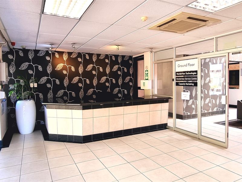 Professional office reception area featuring a built-in service counter, tiled flooring, recessed ceiling lighting, and glass partition doors leading to office suites.
