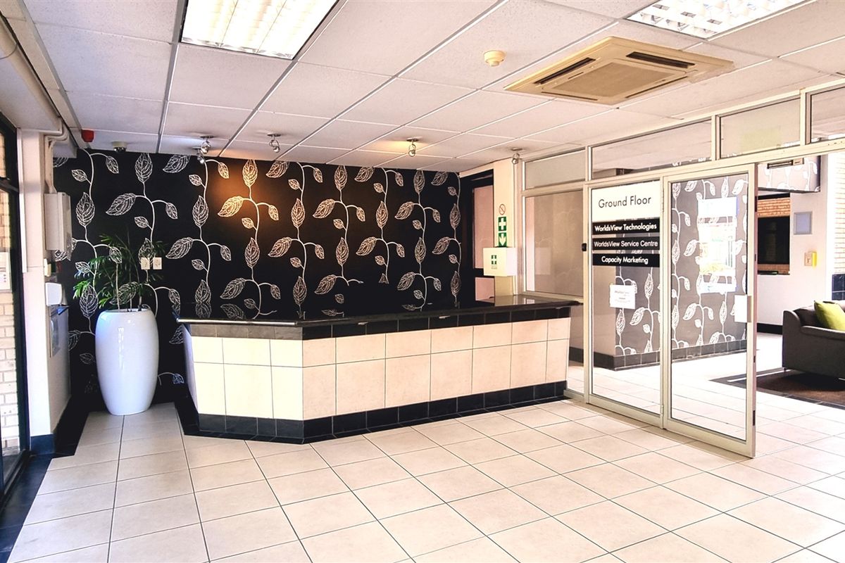 Professional office reception area featuring a built-in service counter, tiled flooring, recessed ceiling lighting, and glass partition doors leading to office suites.
