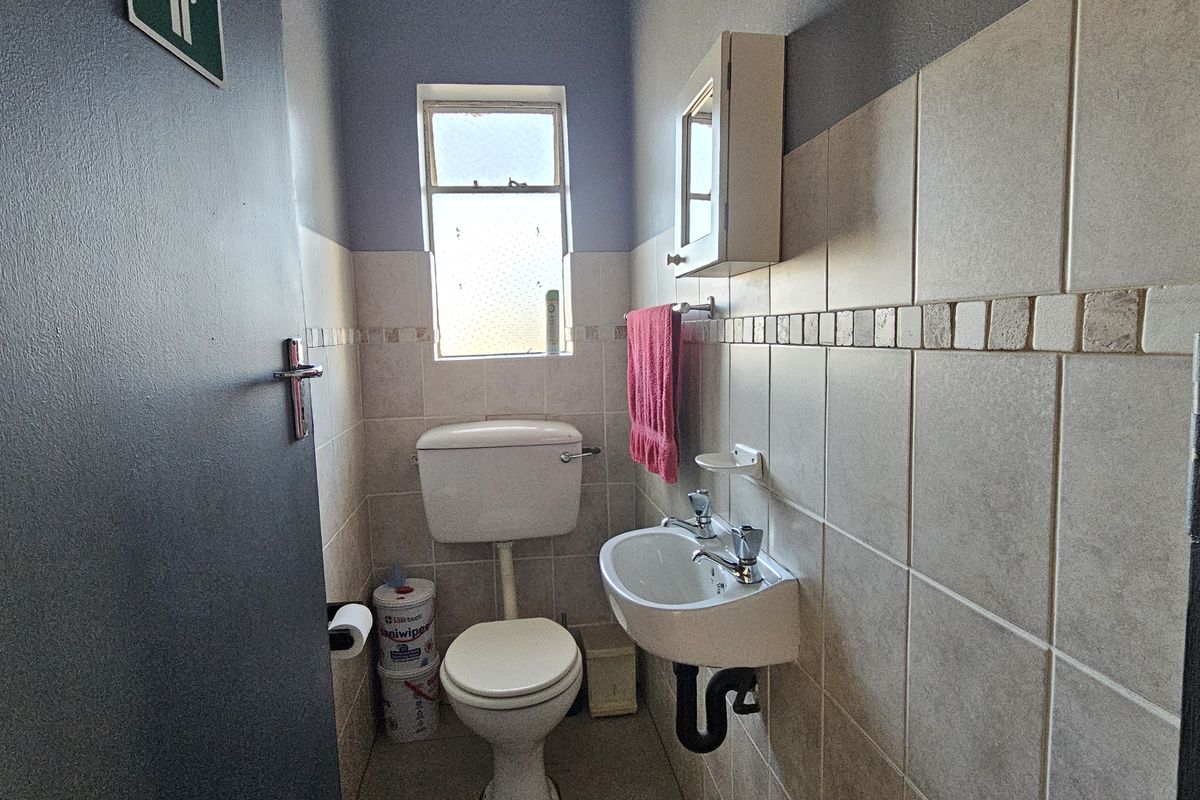 A compact guest bathroom featuring a wall-mounted basin, toilet, and tiled walls with a small window for natural light.