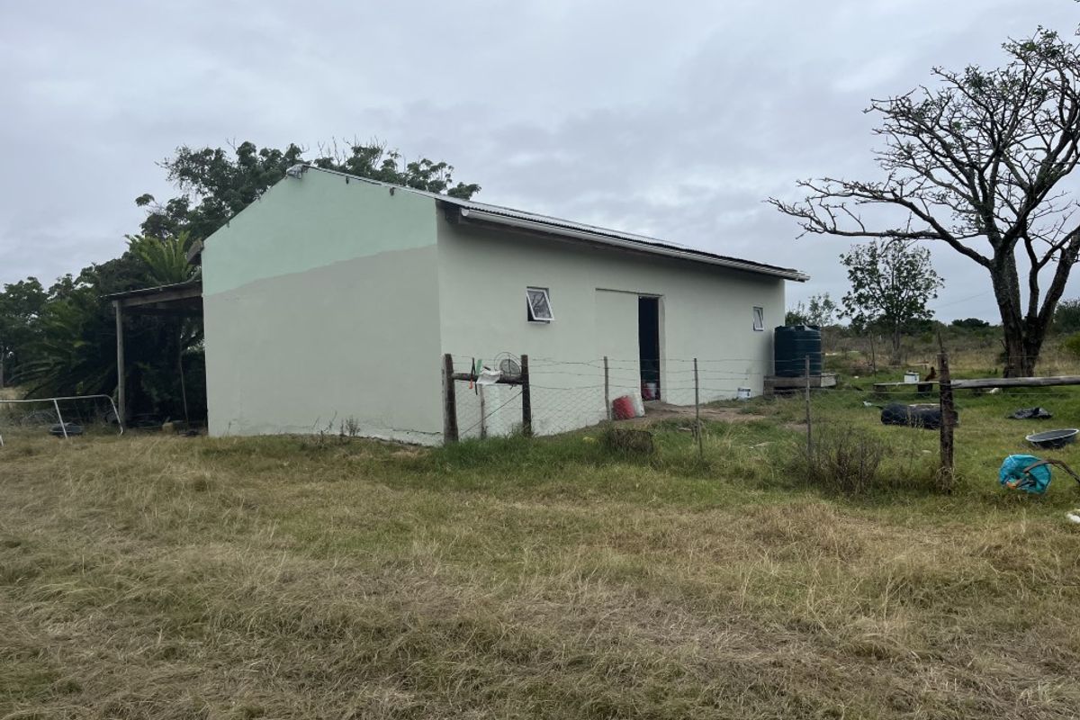 Rear view of a farm outbuilding featuring a corrugated metal roof, exterior water tank, and surrounding wire fencing on a rural property.