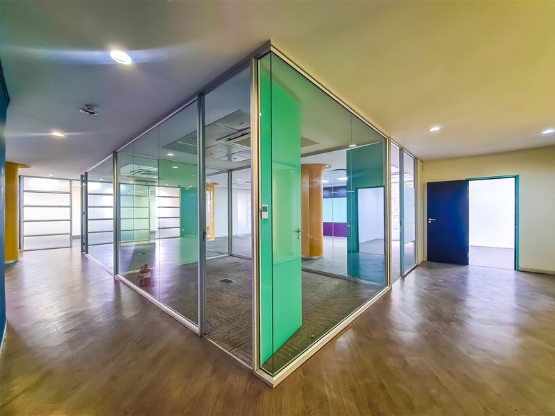 Modern office space featuring glass-partitioned meeting rooms, suspended ceilings, recessed lighting, and a combination of carpet and laminate flooring.