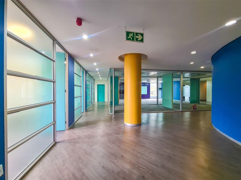 A bright, open-plan office space featuring modern glass partitions, laminate flooring, and a prominent yellow structural column.