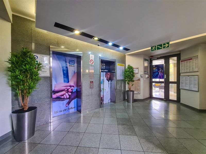 A professional office building lobby featuring a granite-clad elevator bank, tiled flooring, and recessed lighting, providing a clean and functional entrance area.