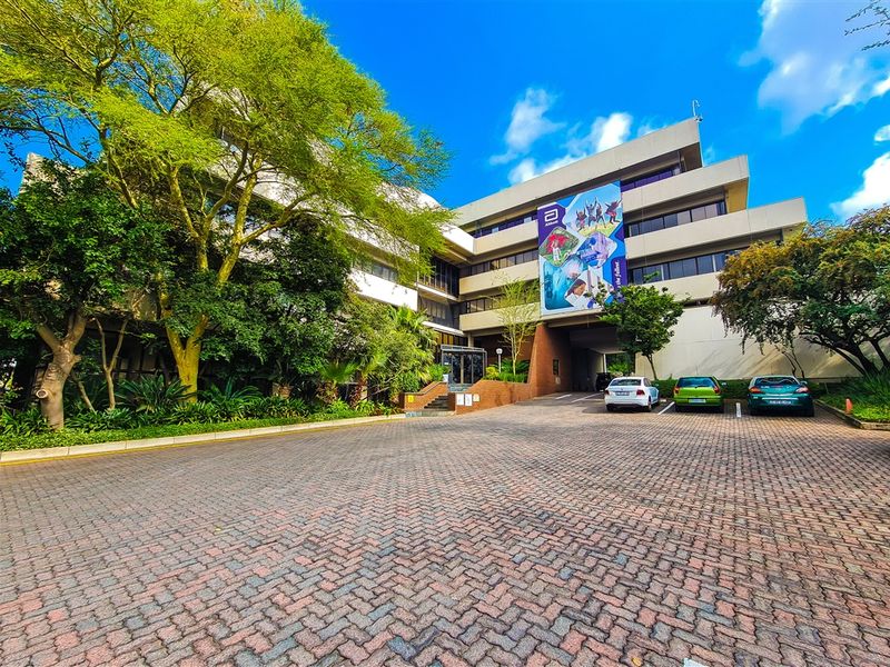 Front exterior view of a multi-story office building featuring a paved driveway, mature landscaping, and a covered parking area.