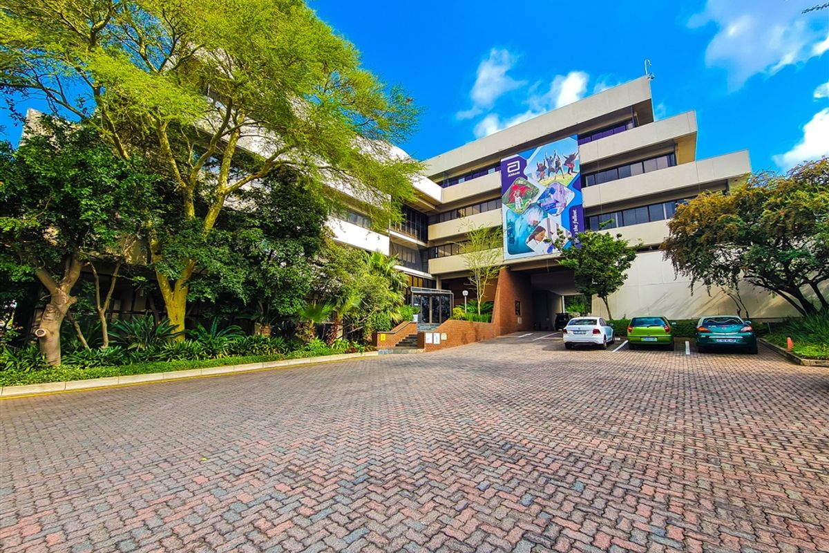 Front exterior view of a multi-story office building featuring a paved driveway, mature landscaping, and a covered parking area.
