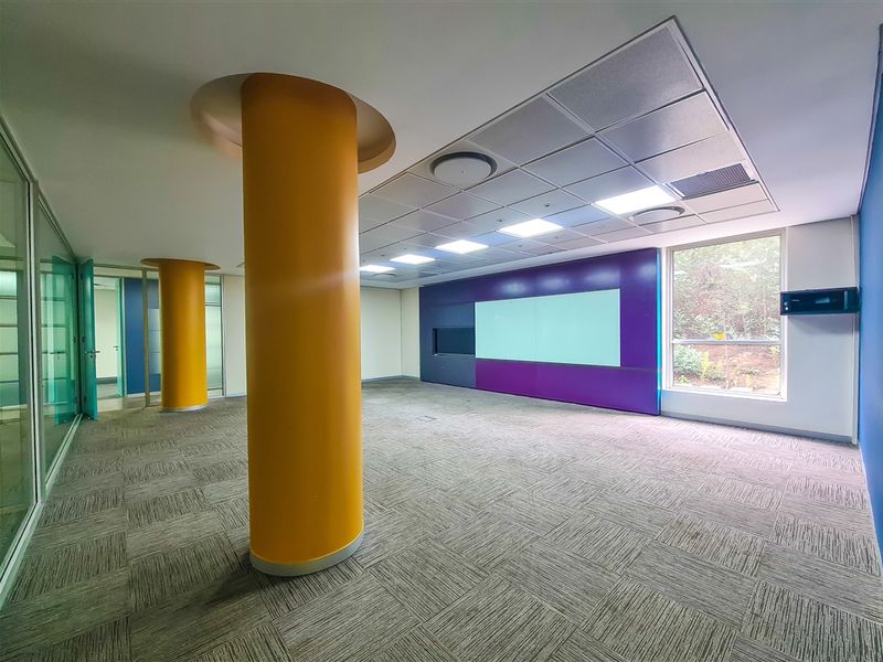 Spacious, modern office area featuring carpet tiles, suspended ceilings with recessed lighting, structural columns, and glass partitioning, offering a bright and professional workspace.