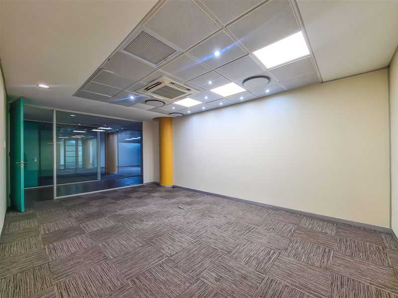 A bright, empty office space featuring carpet tiles, a suspended ceiling with integrated lighting and air conditioning, and a modern glass partition wall.