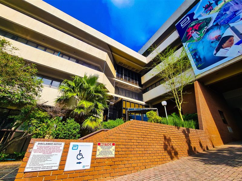 Exterior view of a multi-story office building featuring a brick retaining wall, paved entrance area, and corporate branding signage.