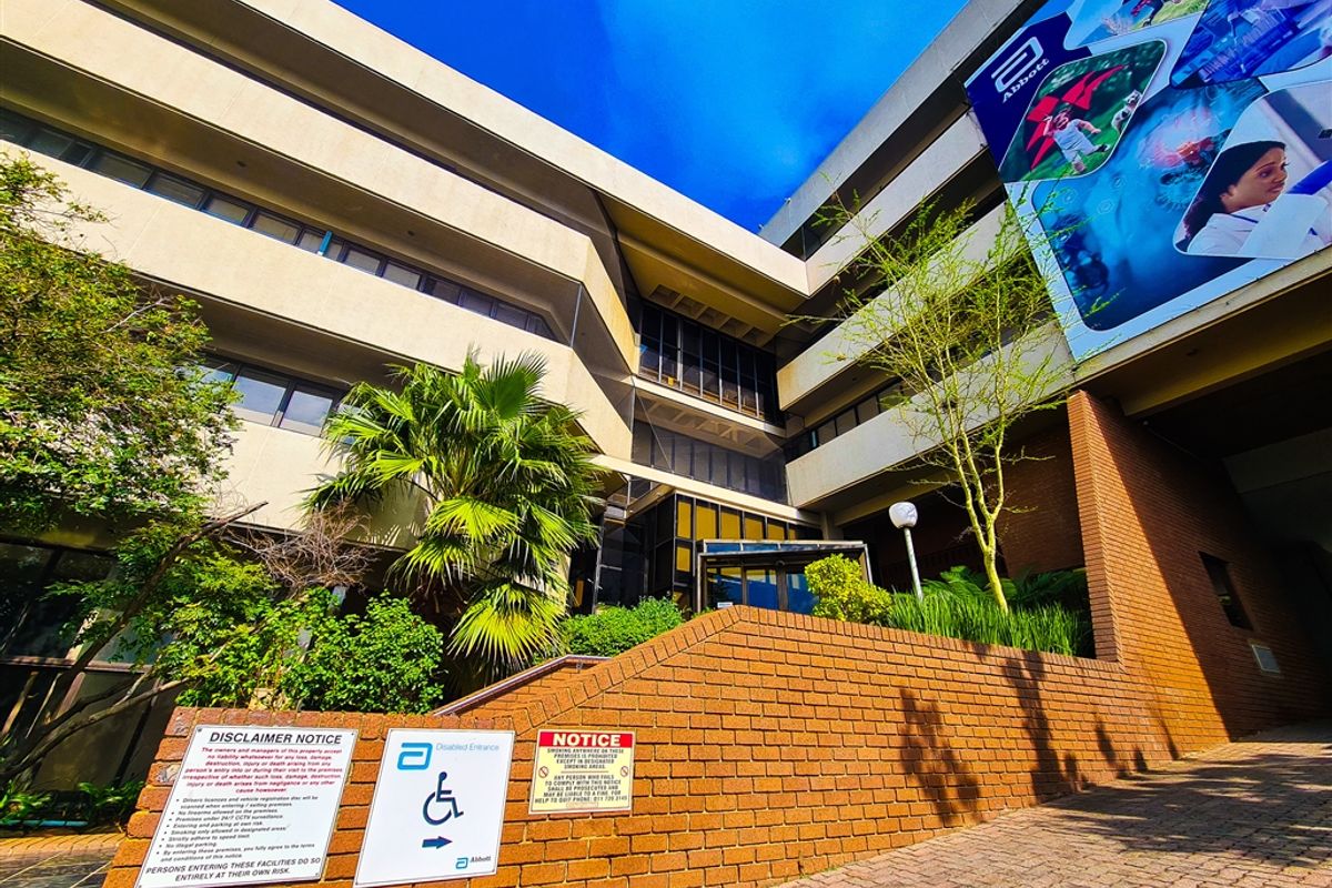 Exterior view of a multi-story office building featuring a brick retaining wall, paved entrance area, and corporate branding signage.