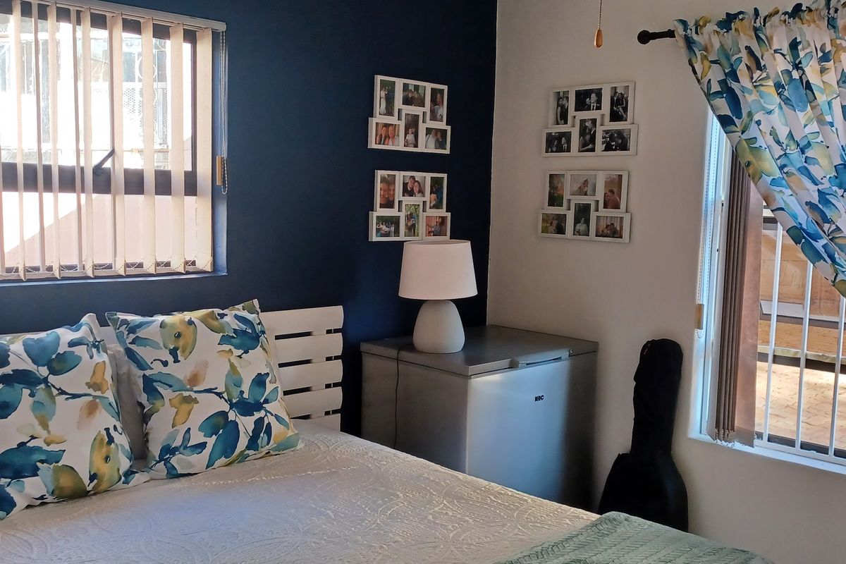 A bedroom featuring an accent wall, vertical blinds, and security bars on the windows, providing a functional and private sleeping space.