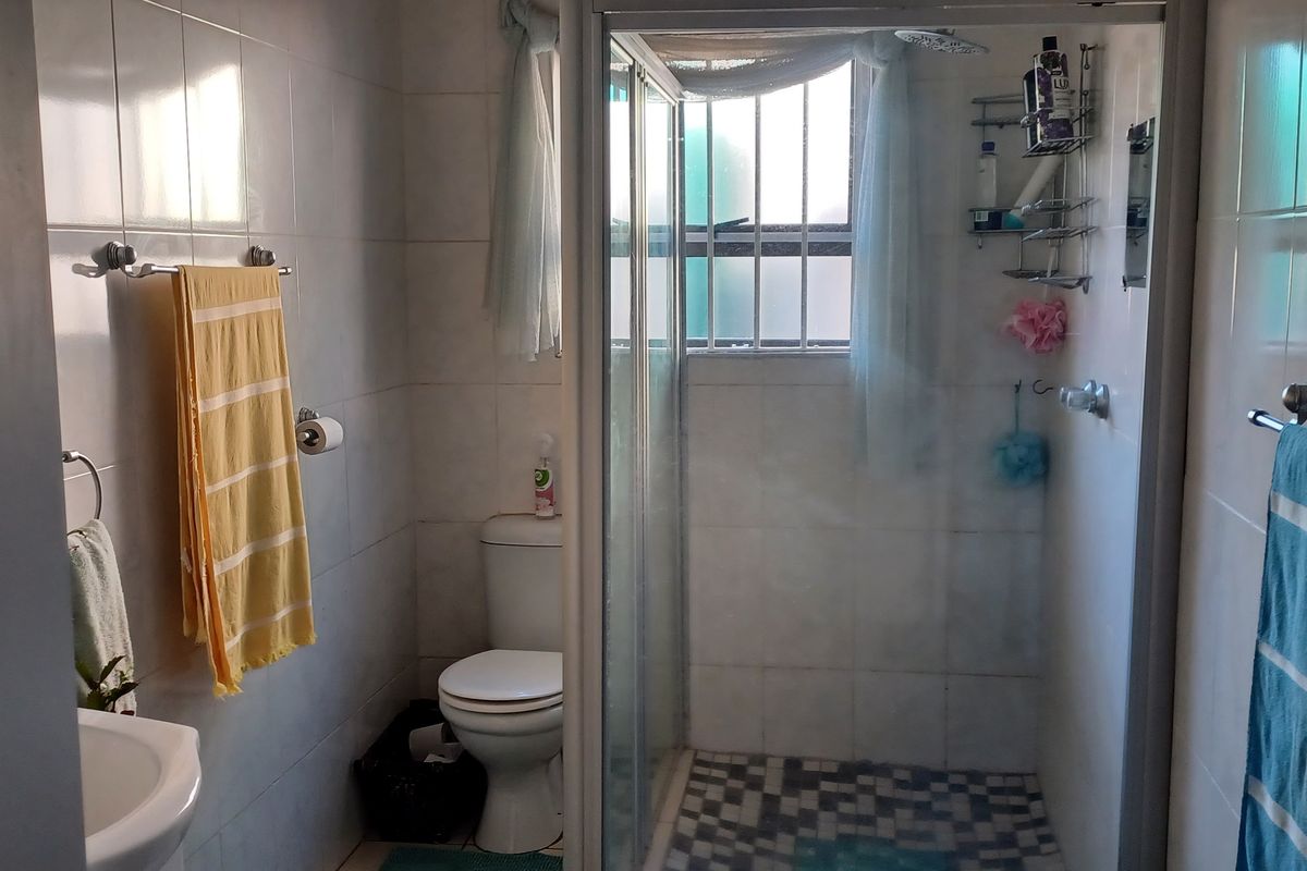 A functional bathroom featuring a glass-enclosed shower, pedestal basin, and toilet with neutral wall tiling and a mosaic-tiled shower floor.