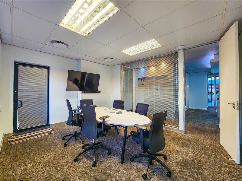 A professional office meeting room featuring a glass partition wall, suspended ceiling with recessed lighting, and carpeted flooring.