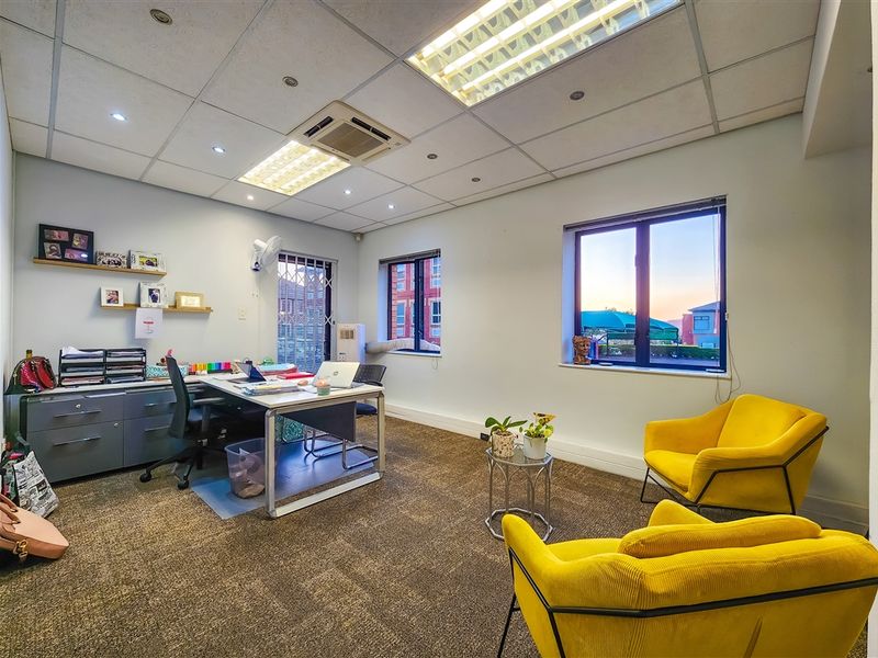 A well-lit office space featuring a suspended ceiling with integrated lighting, ducted air conditioning, carpeted flooring, and large windows with security bars.