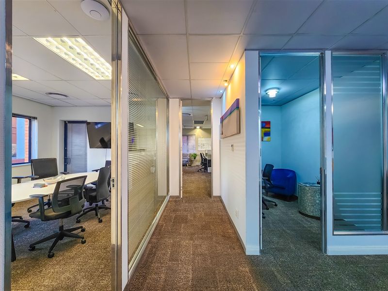 A modern office interior featuring glass partition walls, carpeted flooring, and suspended ceilings with recessed lighting, creating a professional and functional workspace environment.