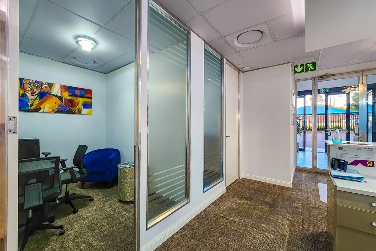 Professional office space featuring glass partitions, carpeted flooring, a reception area, and a suspended ceiling with integrated lighting.