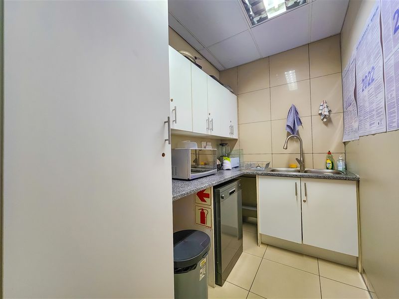 A compact office kitchenette featuring built-in cabinetry, a stainless steel sink, tiled splashbacks, and durable tiled flooring.
