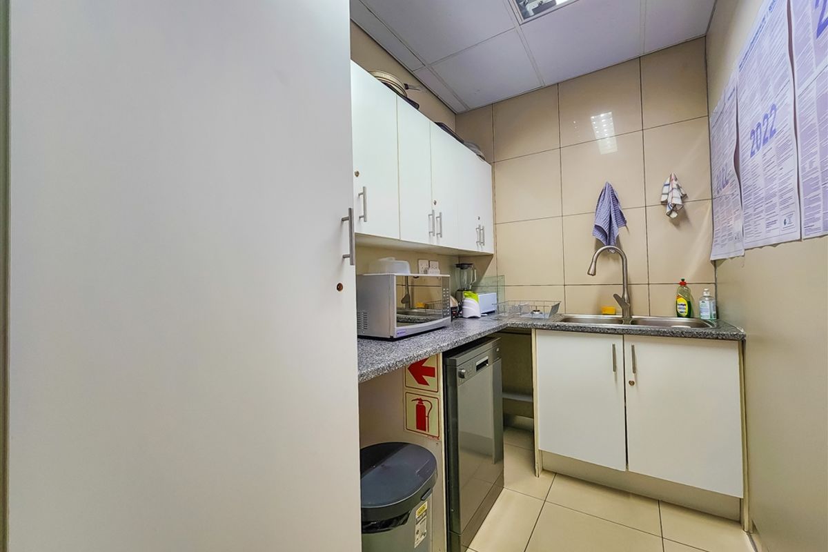 A compact office kitchenette featuring built-in cabinetry, a stainless steel sink, tiled splashbacks, and durable tiled flooring.