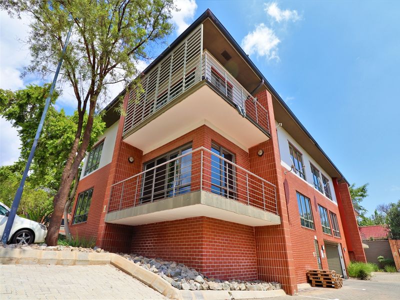 Modern multi-story office building featuring a face brick facade, corner balconies with metal railings, and large aluminium-framed windows.