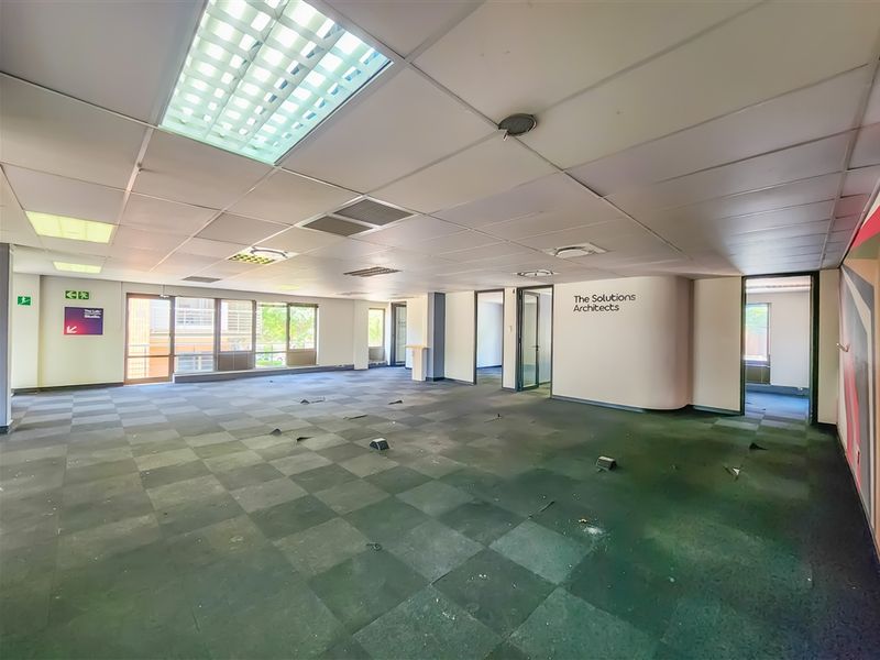 Spacious open-plan office area featuring suspended ceilings, recessed lighting, and large windows, currently vacant and requiring flooring repairs.