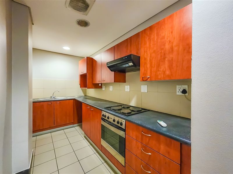 A functional galley-style kitchen featuring wood-finish cabinetry, integrated electric oven and hob, tiled backsplash, and durable tiled flooring.