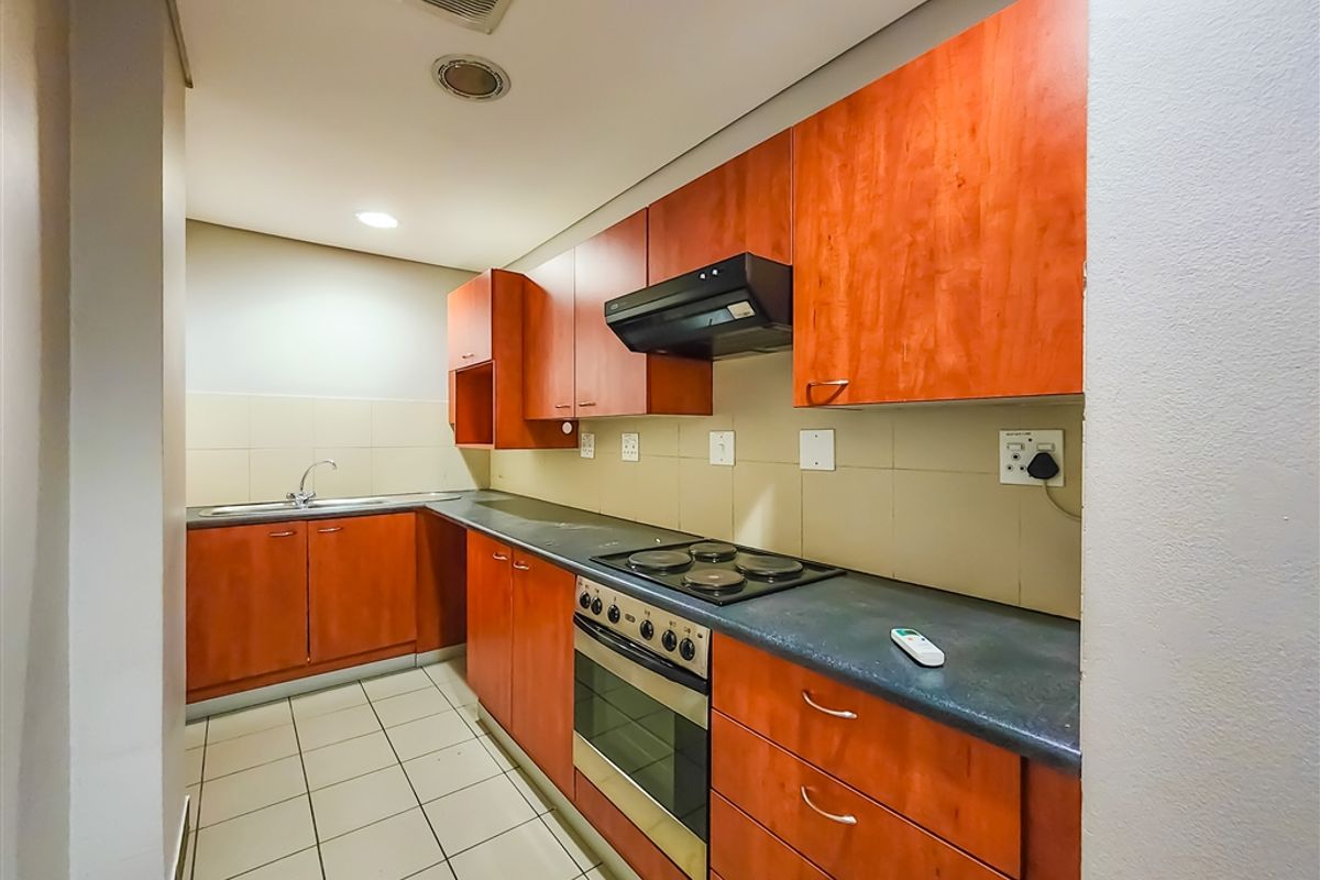 A functional galley-style kitchen featuring wood-finish cabinetry, integrated electric oven and hob, tiled backsplash, and durable tiled flooring.