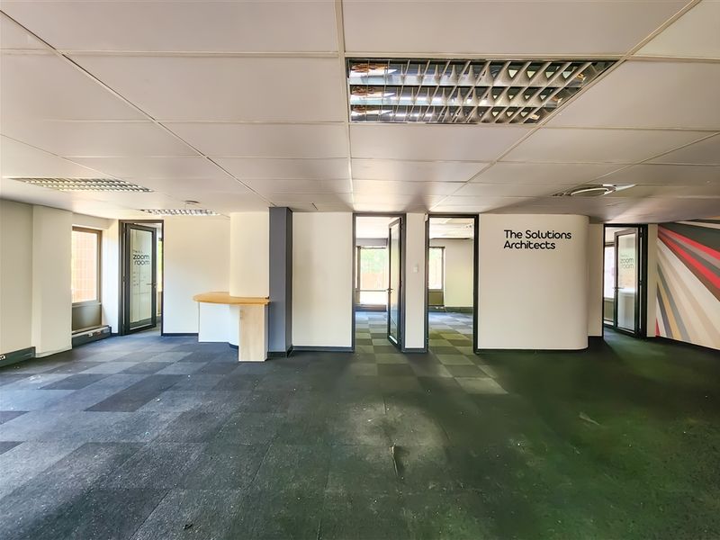 Open plan office space featuring suspended ceilings, recessed lighting, and carpet tiles, with multiple partitioned office rooms accessible through glass doors.
