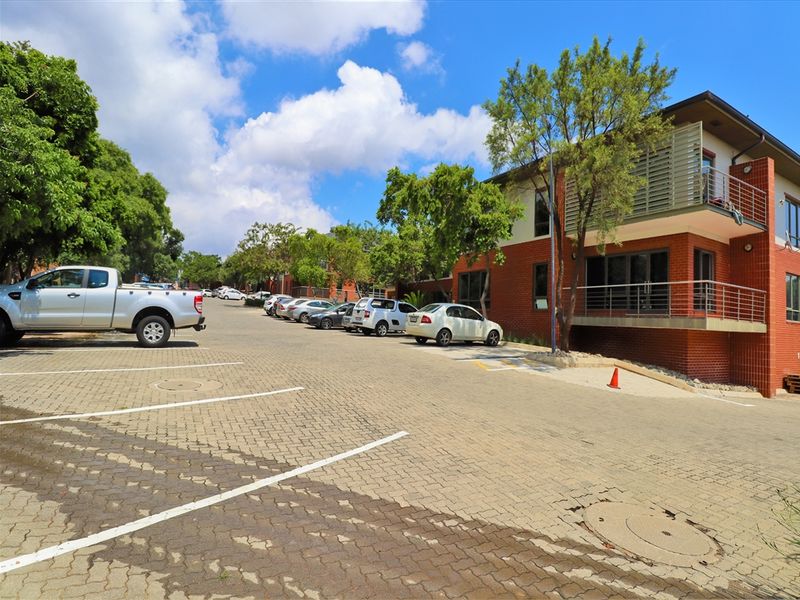 Exterior view of an office building featuring a brick facade, paved parking area, and a balcony with metal railings.