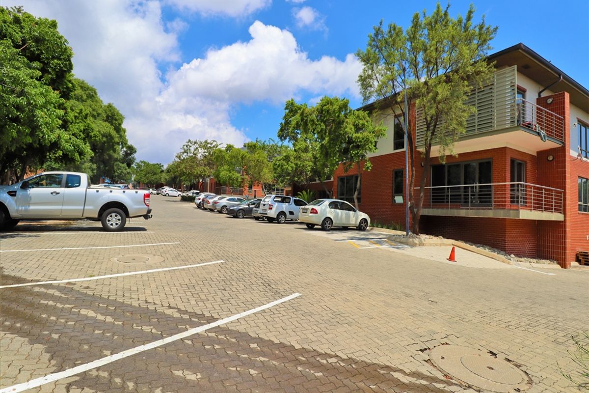 Exterior view of an office building featuring a brick facade, paved parking area, and a balcony with metal railings.