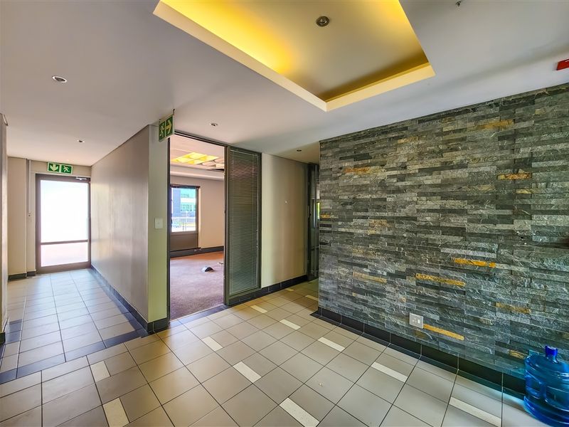 A modern office hallway featuring a decorative stone accent wall, recessed ceiling lighting, and tiled flooring leading into an adjacent office space.